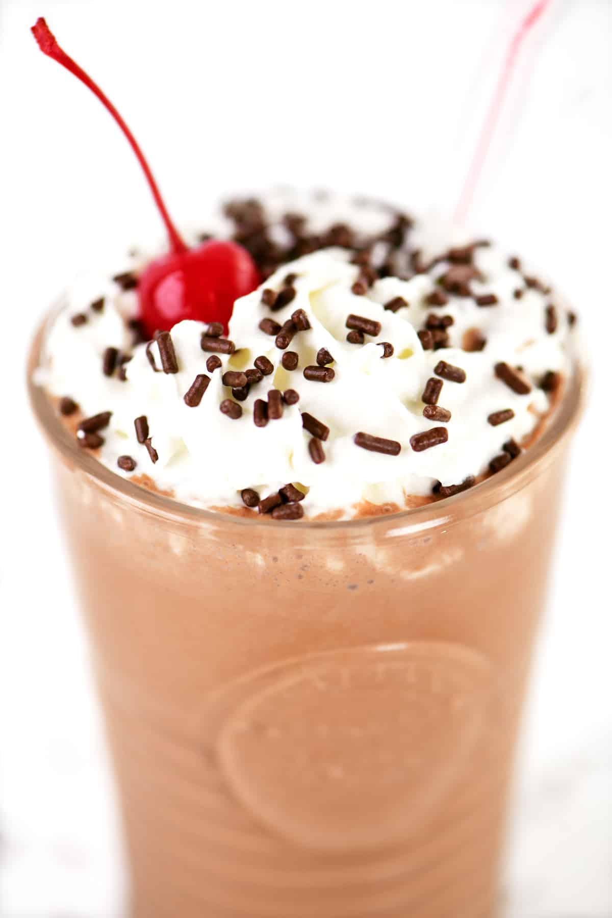 A chocolate milkshake garnished with whipped cream, sprinkles and a cherry.