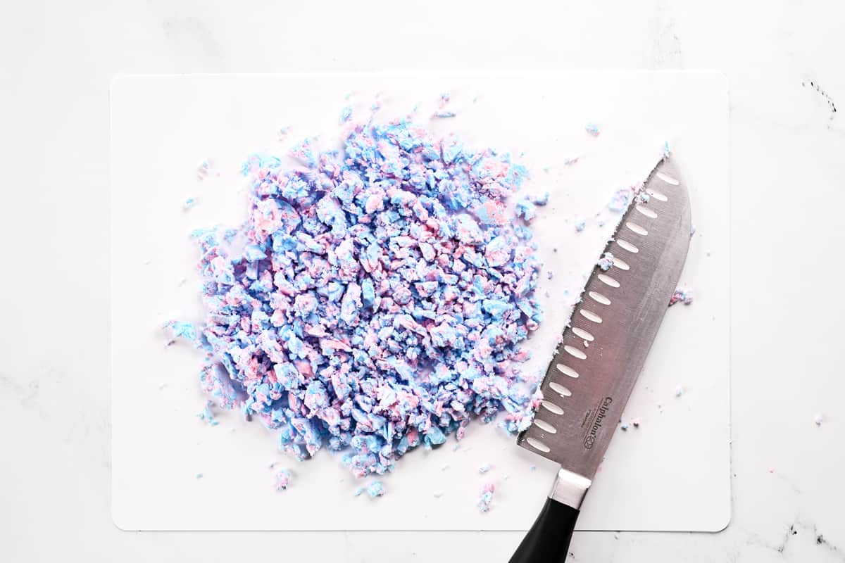 A knife and chopped cotton candy on a paper cutting board.