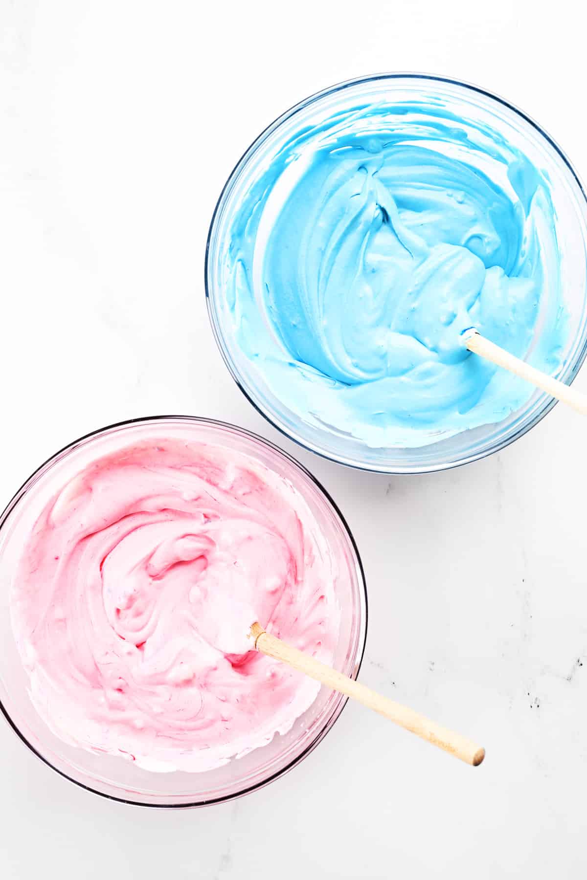 Pink and blue ice cream mixture in mixing bowls.
