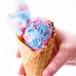 A hand holding a waffle cone with cotton candy ice cream inside.
