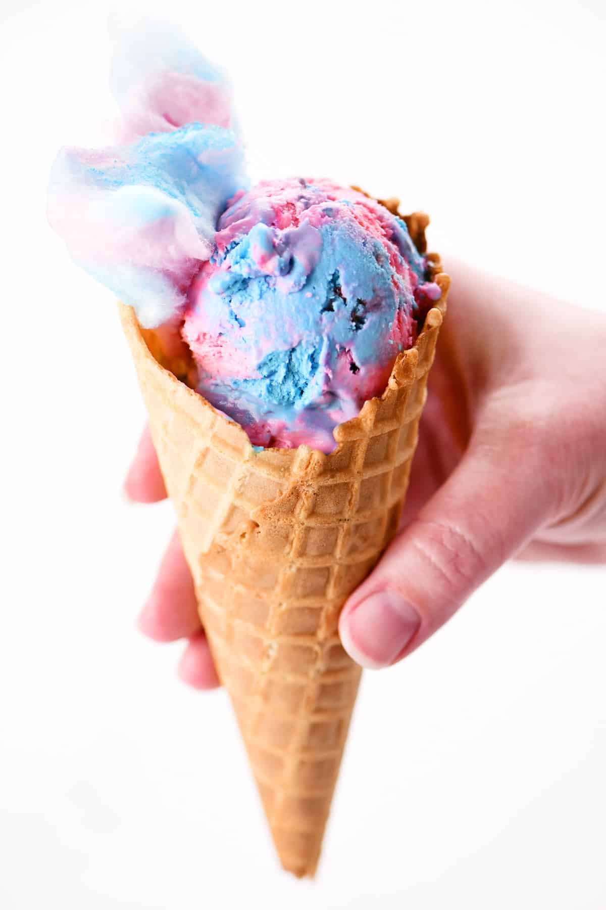 Cotton candy ice cream that is blue and pink in a waffle cone.