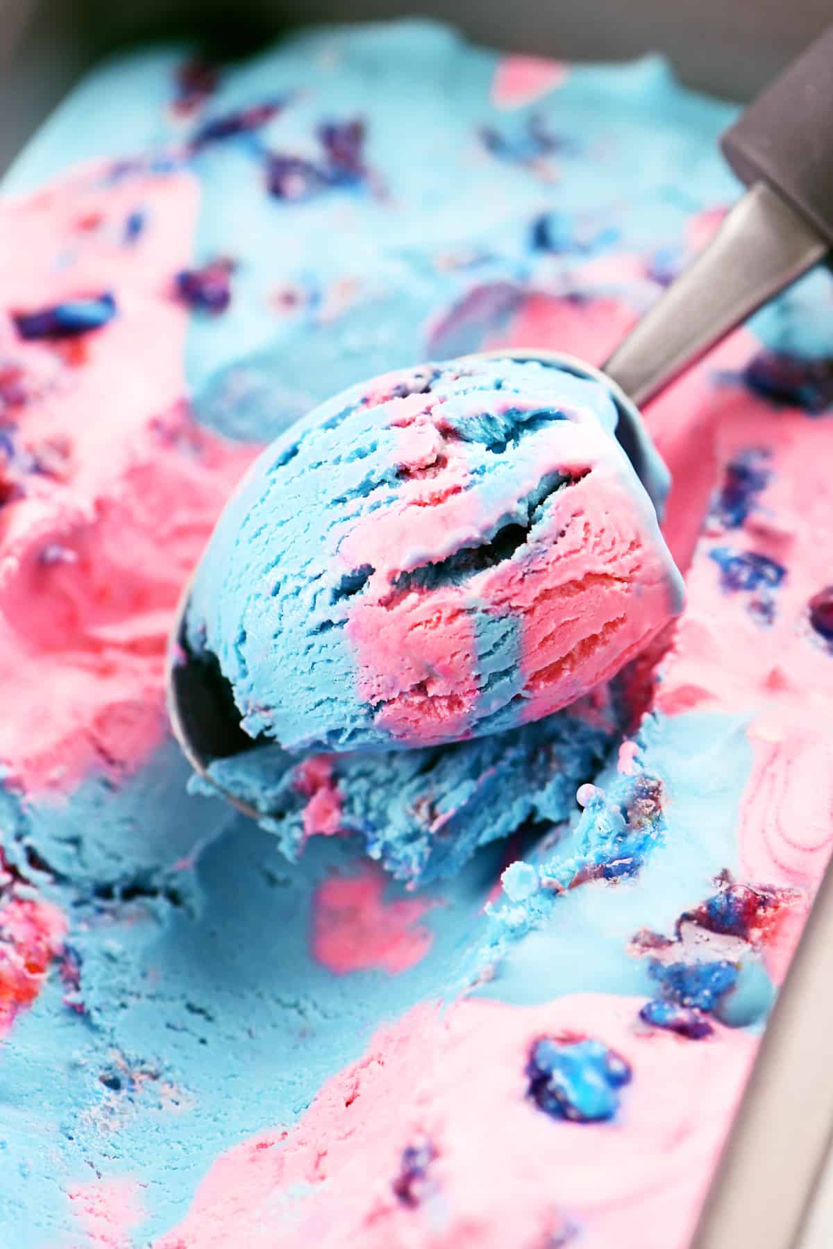 An ice cream scooper is scooping pink and blue ice cream from a loaf pan.