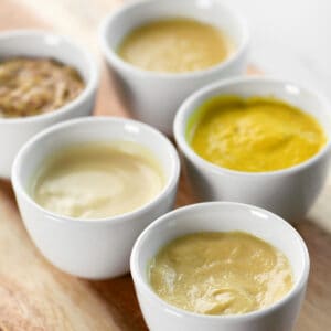 Five different mustard varieties in small white bowls.