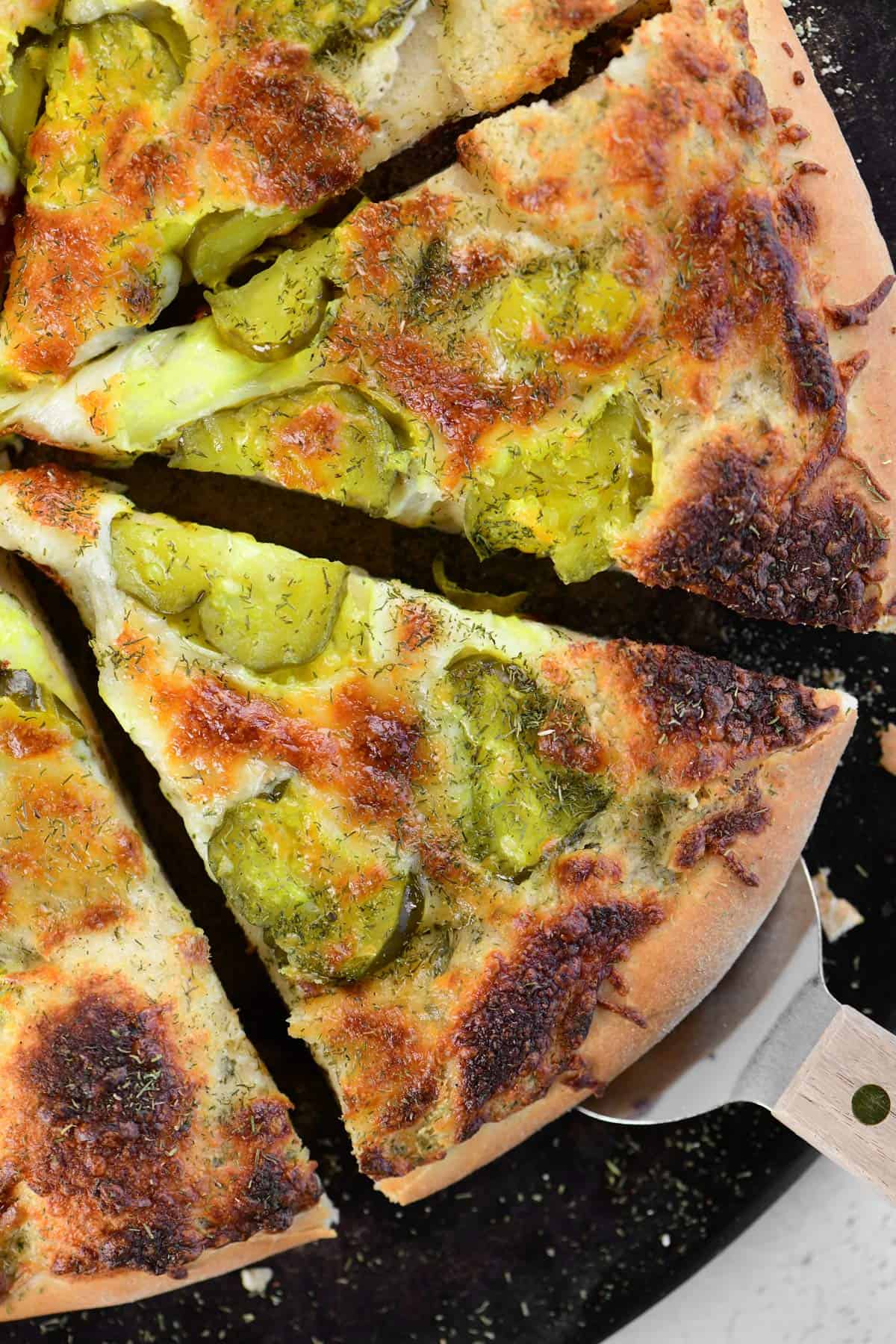 A pizza server removing a slice of dill pickle pizza.
