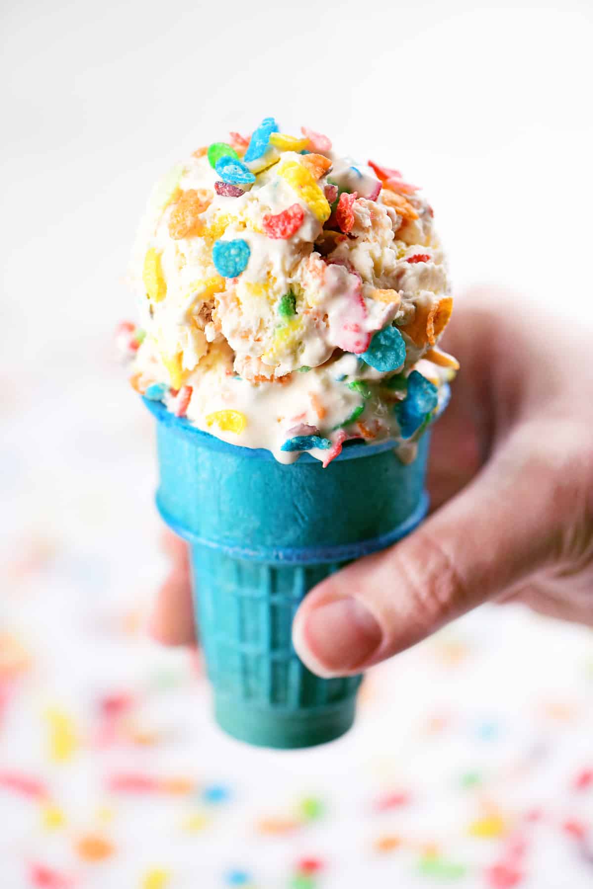A blue cone with scoops of Fruity Pebbles Ice Cream inside.