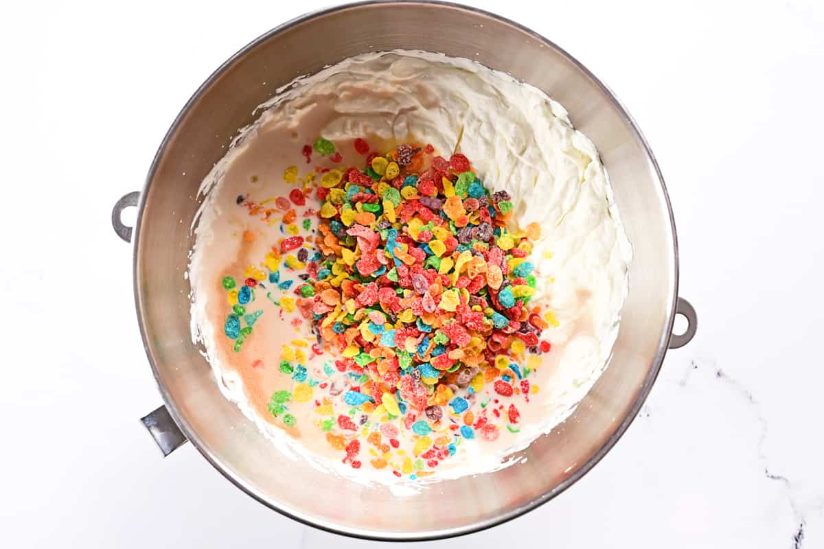 A mixing bowl with heavy whipping cream, condensed milk and Fruity Pebbles inside.