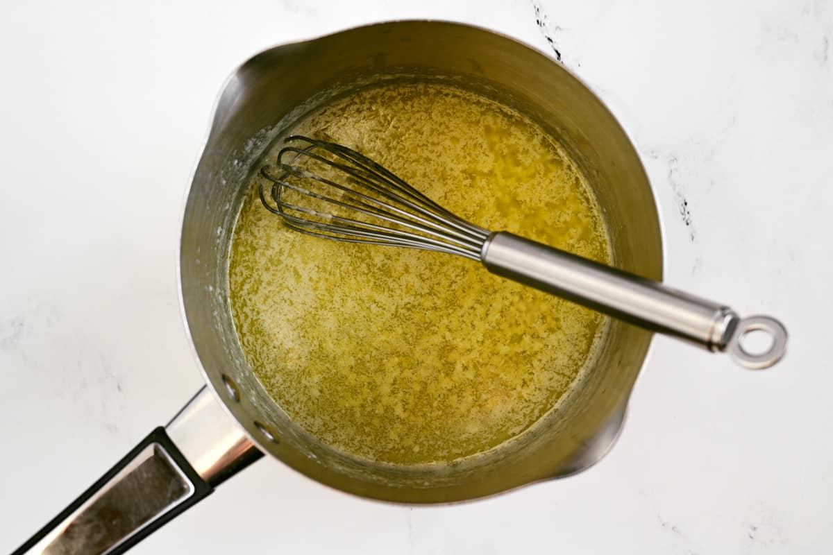 A saucepan with garlic, butter, and a whisk inside.