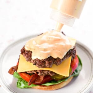 Sauce is applied to a burger from a plastic squeeze bottle.