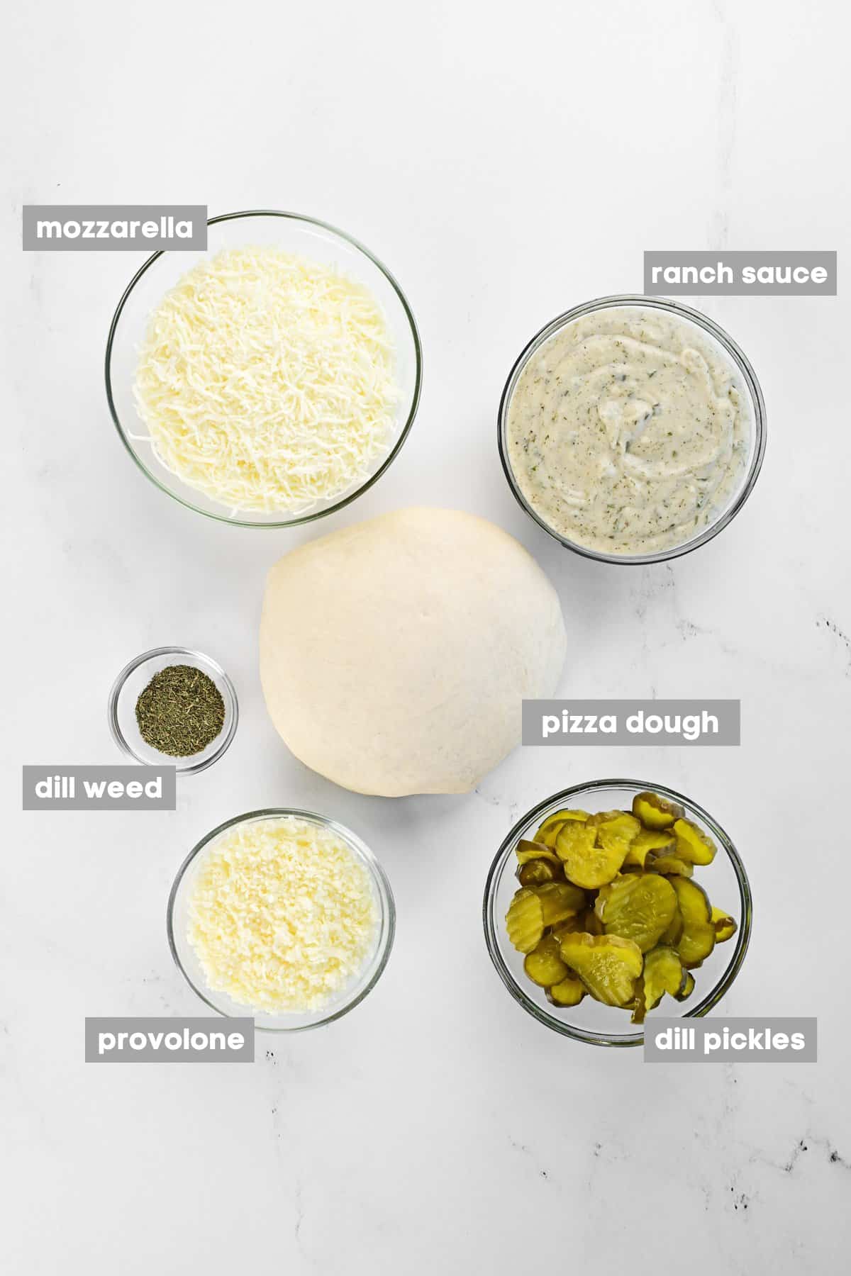 Dough and ingredients in bowls on a marble countertop.