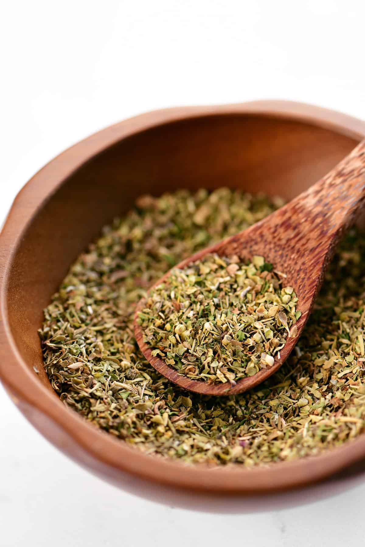 An Italian seasoning substitute mix on a wooden spoon in a bowl filled with seasonings.