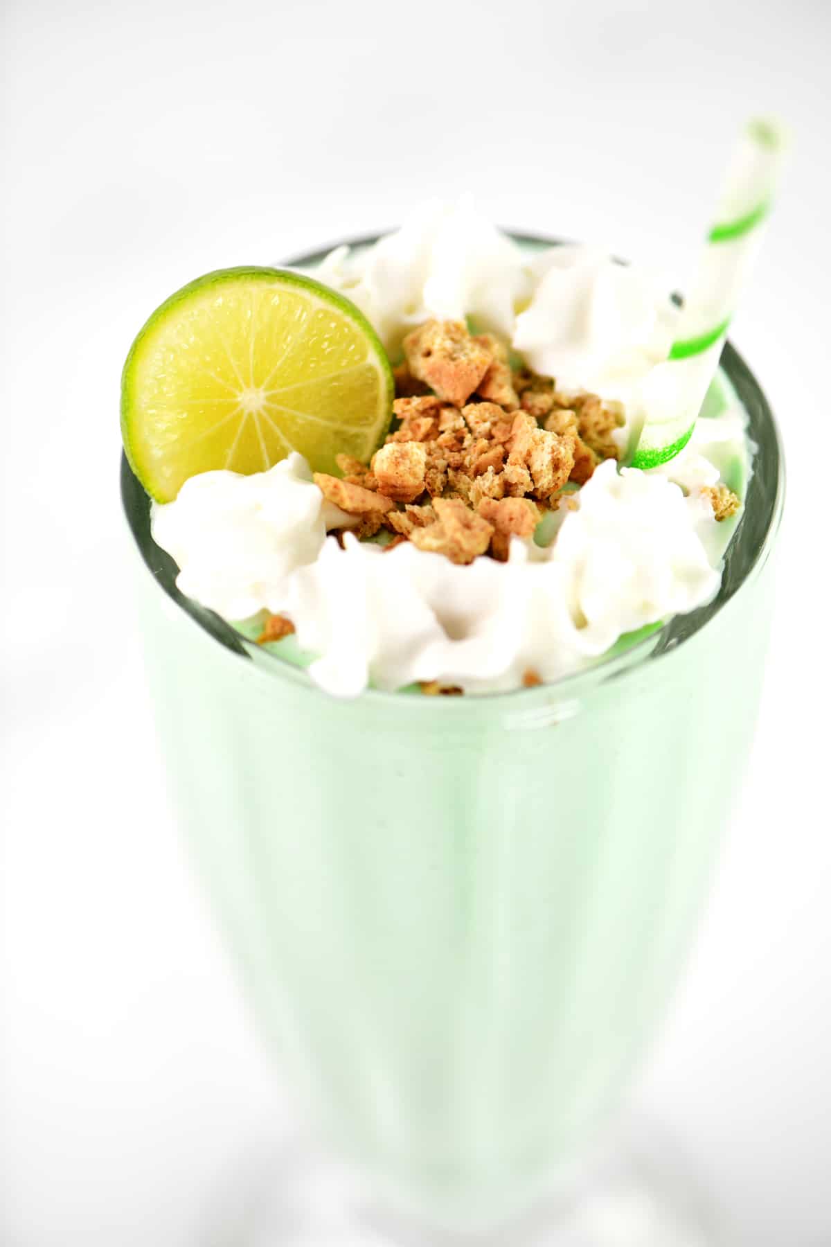 A lime, graham cracker crumbles and whipped cream on top of a key lime milkshake.