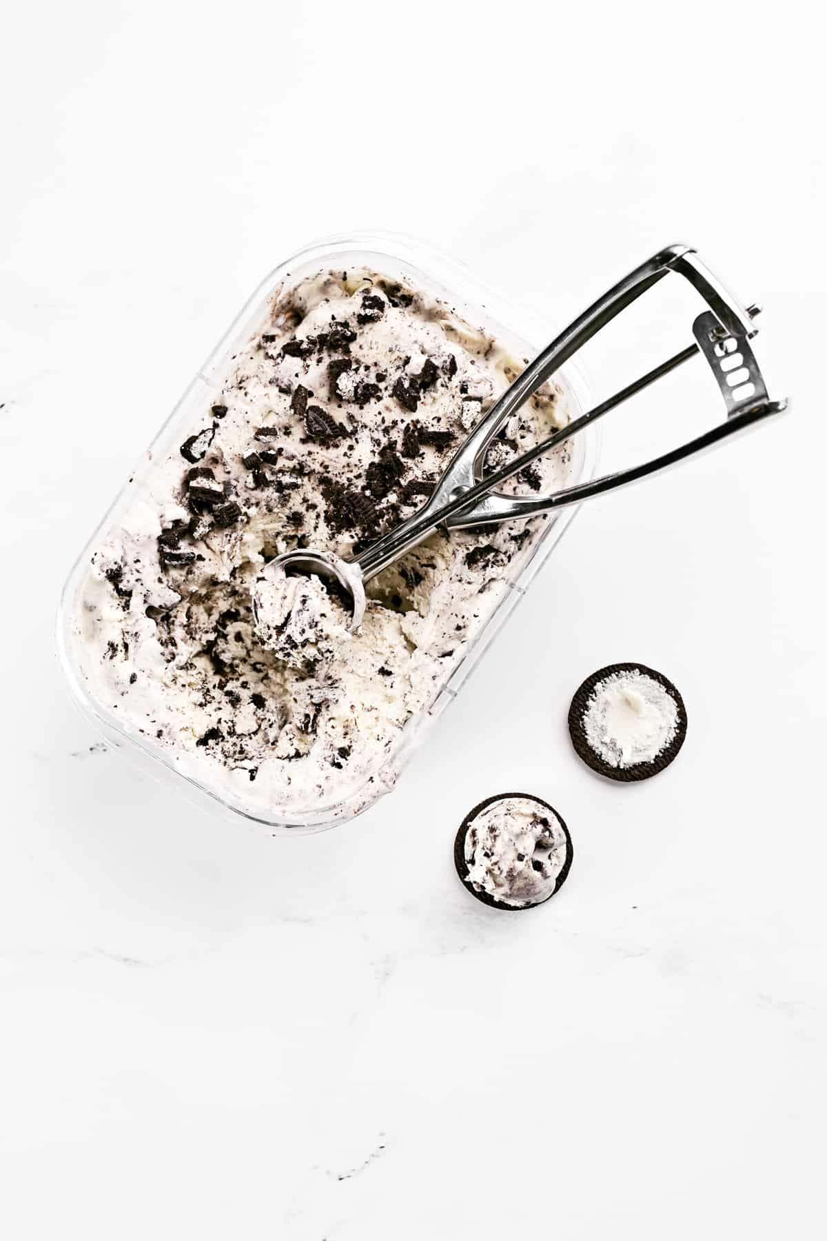 An ice cream scoop in an ice cream container next to an Oreo cookie with a scoop of ice cream on it.