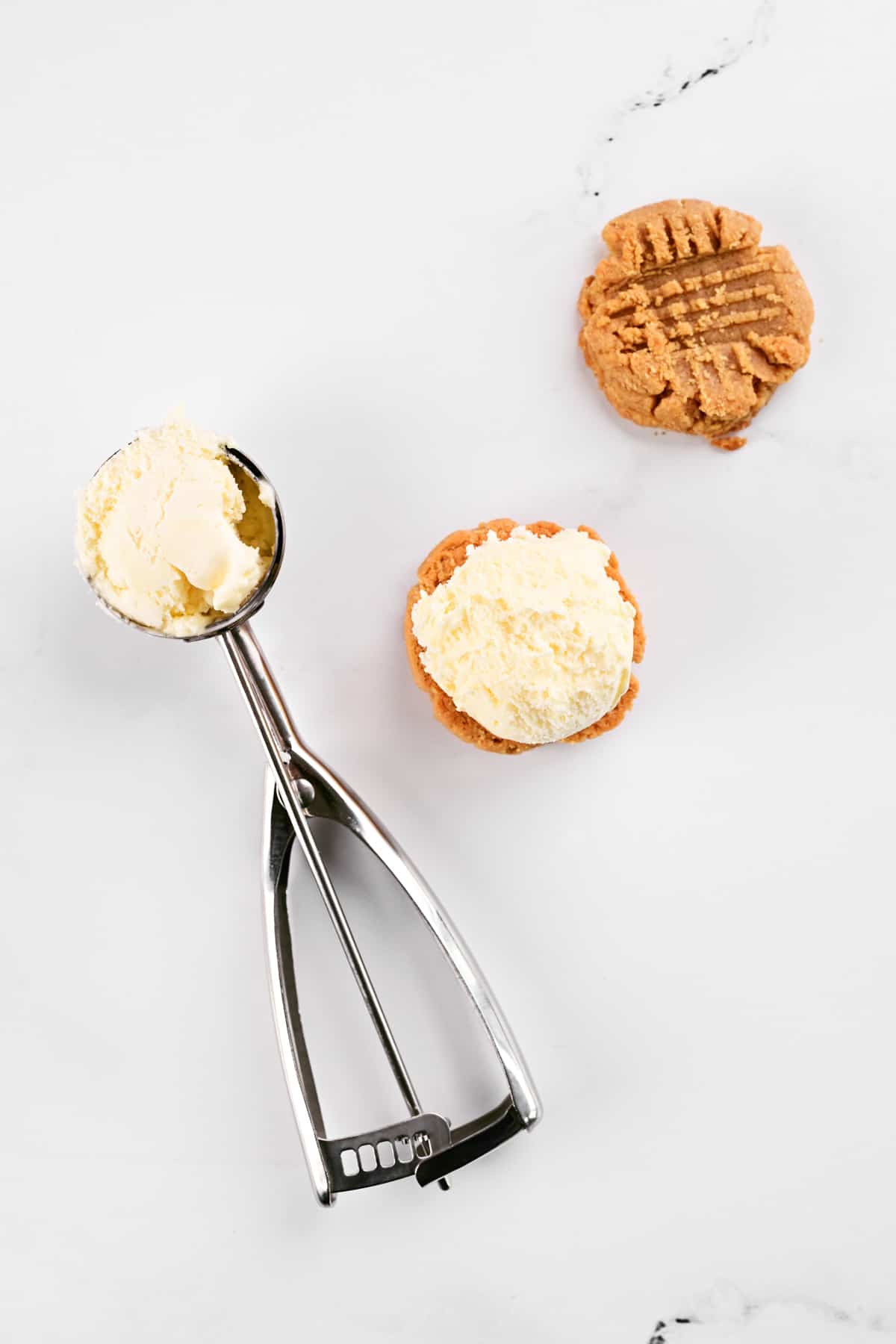 A scoop of ice cream in an ice cream scoop next to cookies and another scoop of vanilla ice cream.