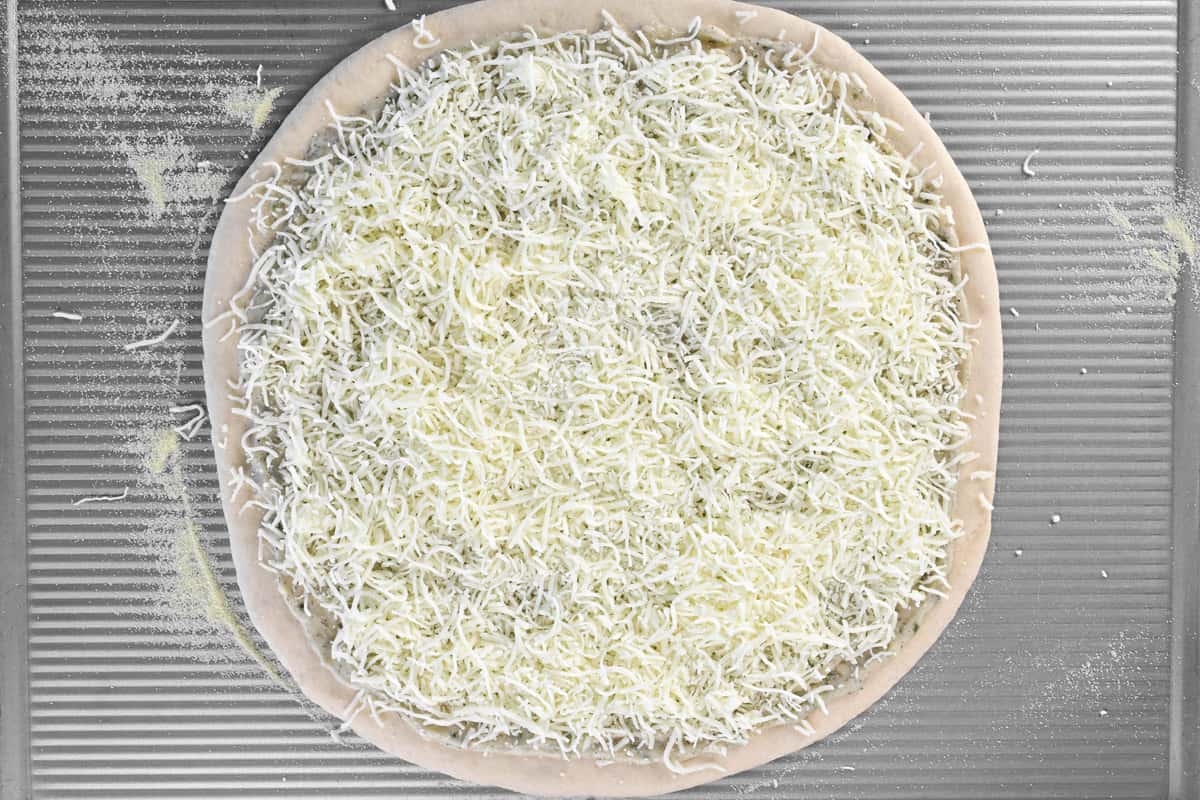A round pizza dough with shredded mozzarella cheese on top.