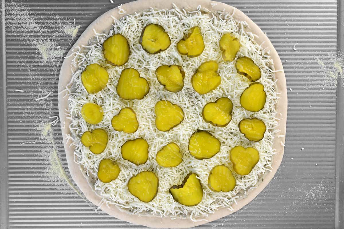 A pizza dough with sauce, cheese, and pickles on top.