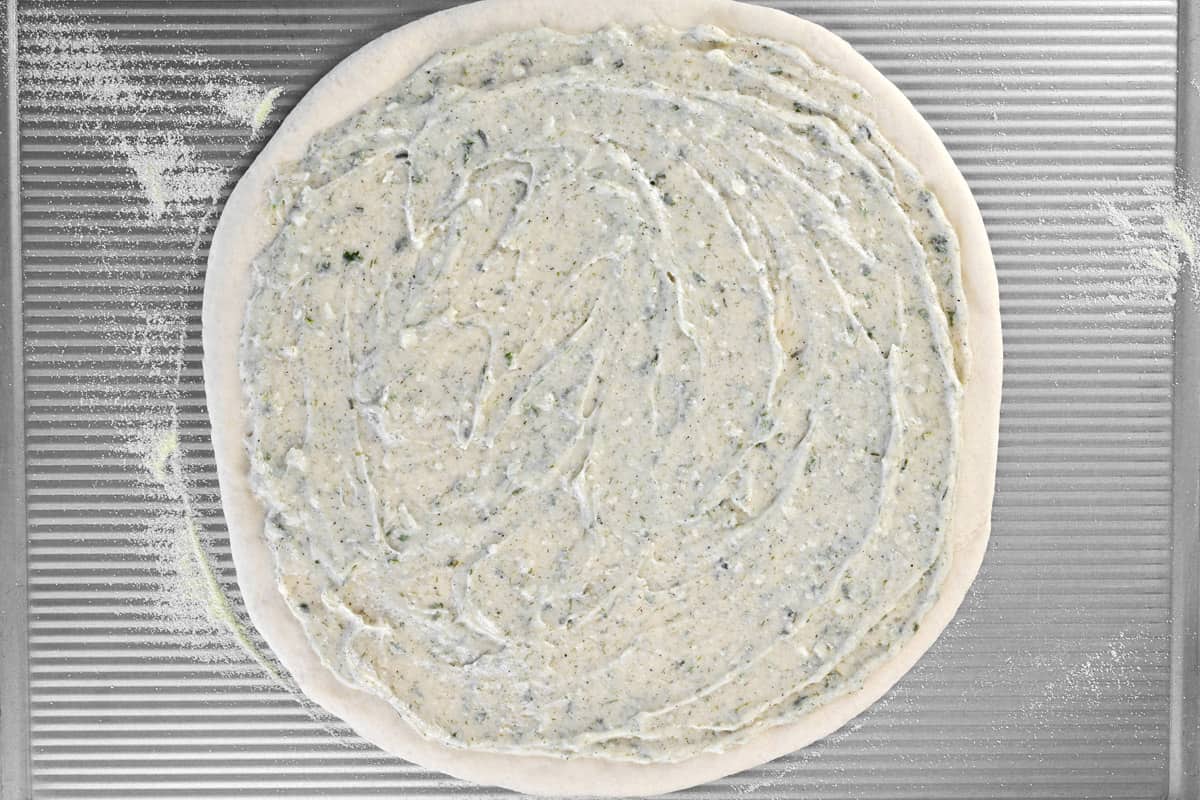 A pizza dough with a dill white sauce on top of it.