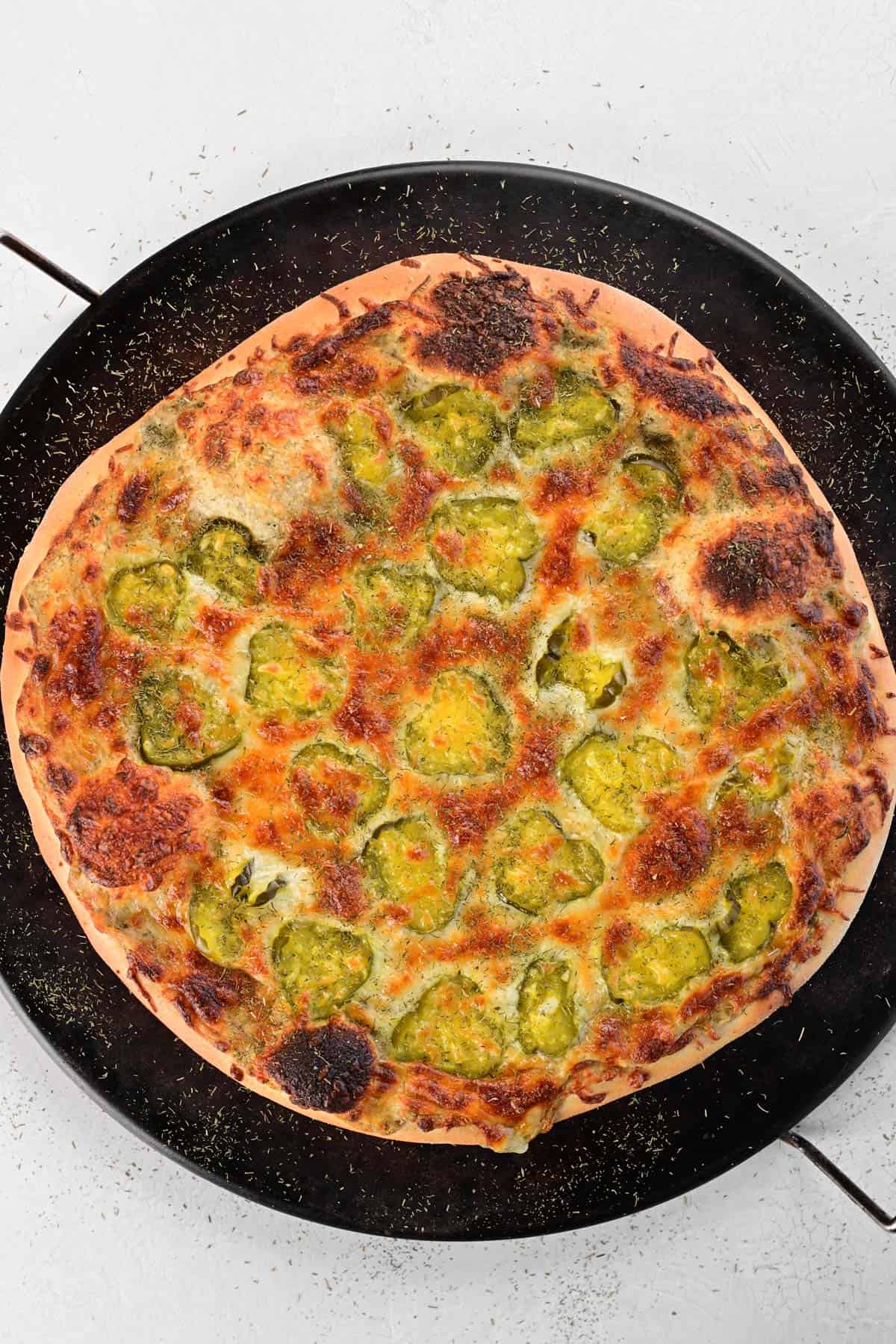 A pizza stone with a pickle pizza sitting on top of it.