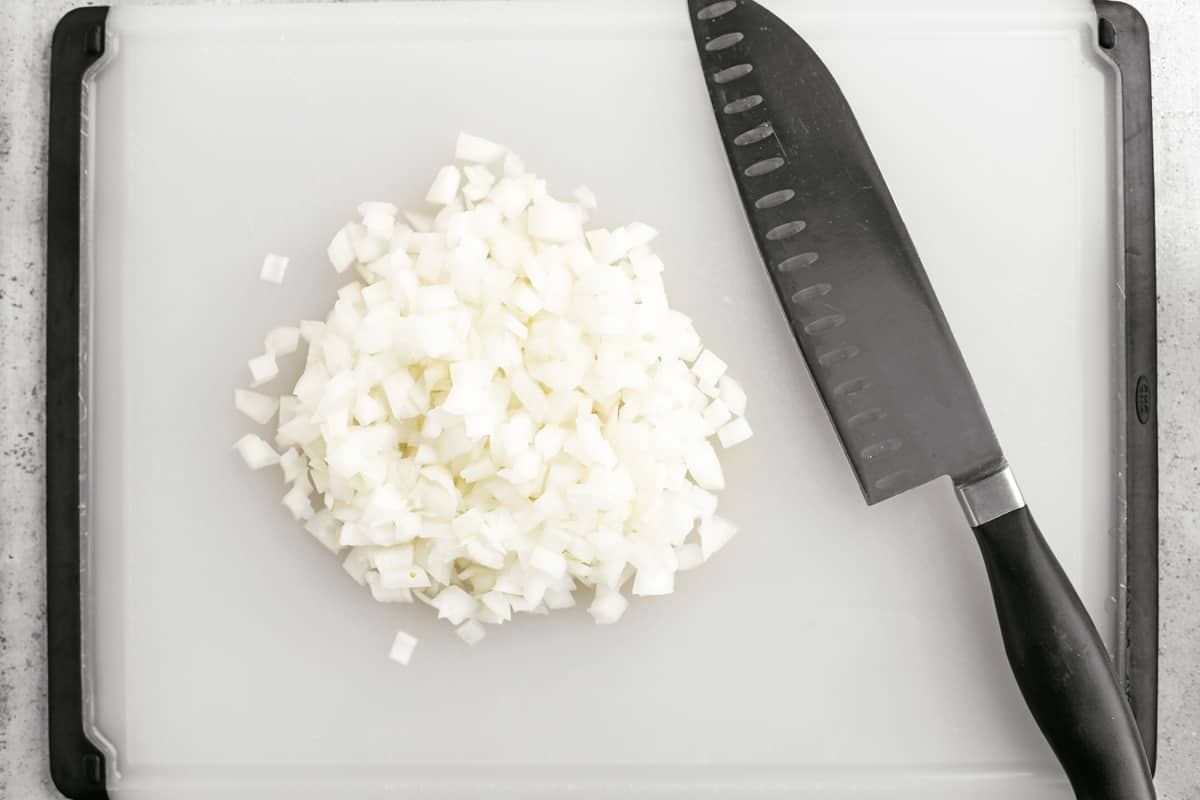 Diced onions and a knife on a cutting board.
