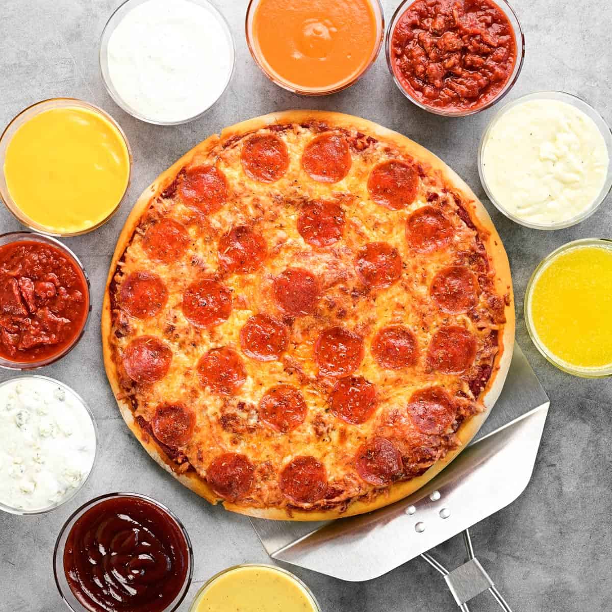 Pizza dipping sauces in bowls surrounding a pepperoni pizza.