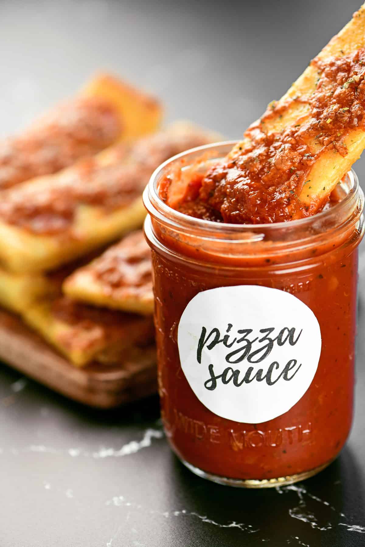 A pizza stick is dipped into a jar of pizza sauce.