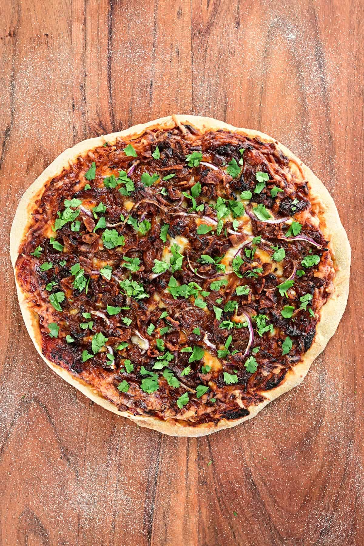 A pulled pork pizza on a wood cutting board.