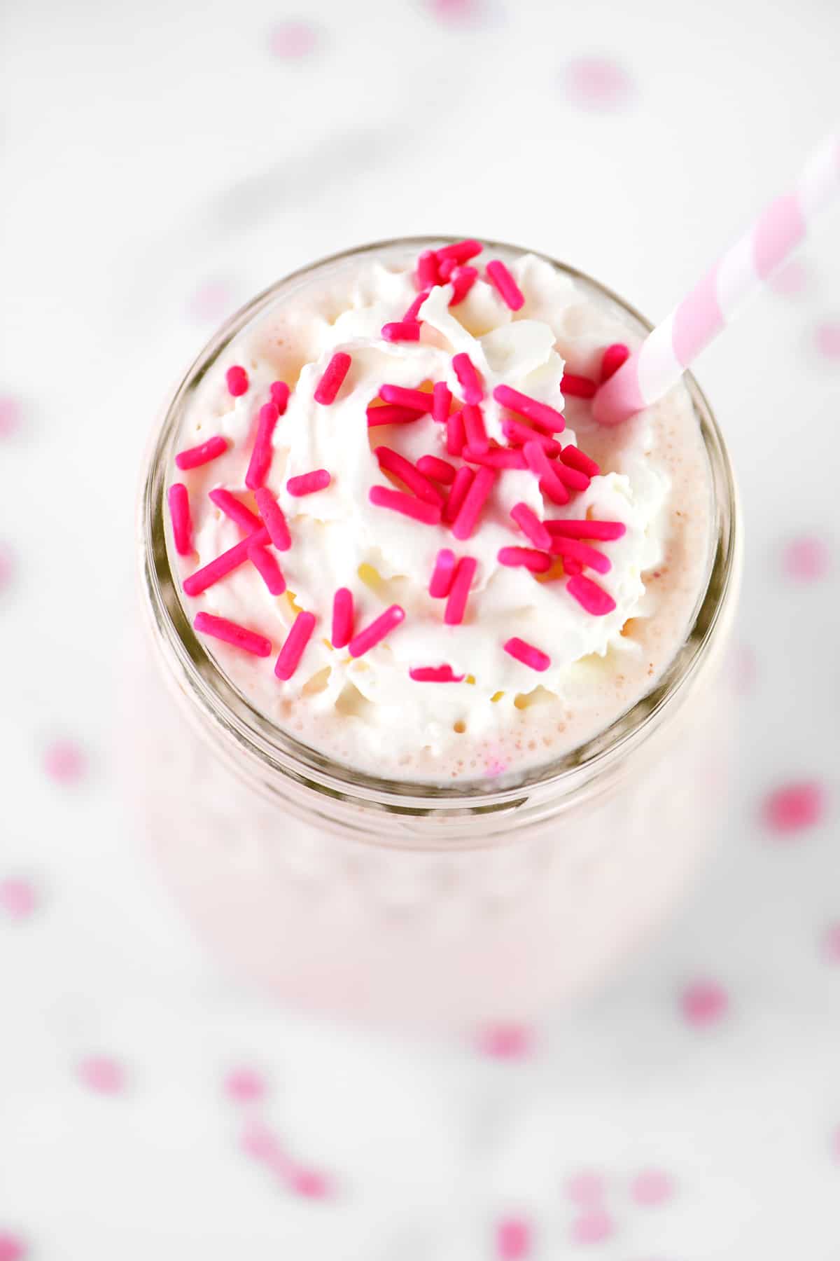 whipped topping, sprinkles and a straw in a strawberry milkshake.
