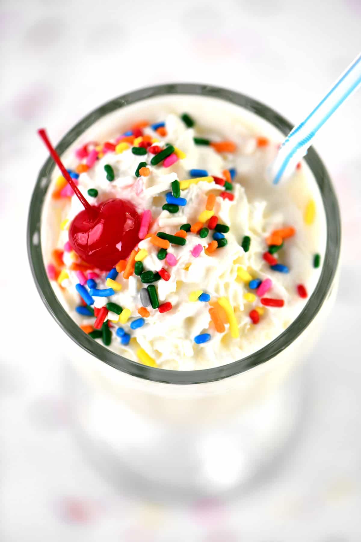 Whipped cream, a cherry and sprinkles on a vanilla milkshake.