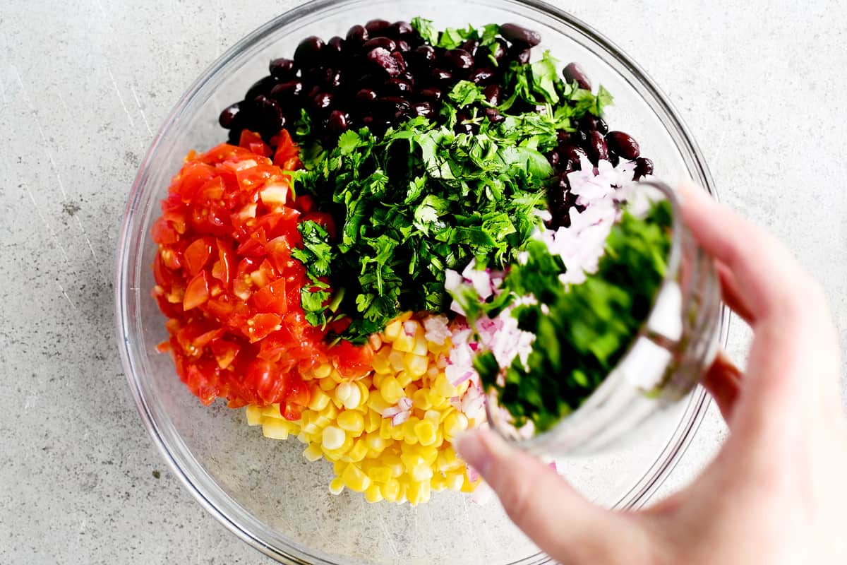Adding cilantro to the bowl of chopped ingredients.