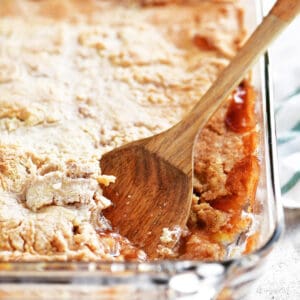 A wooden spoon and apple cobbler in a glass baking dish.