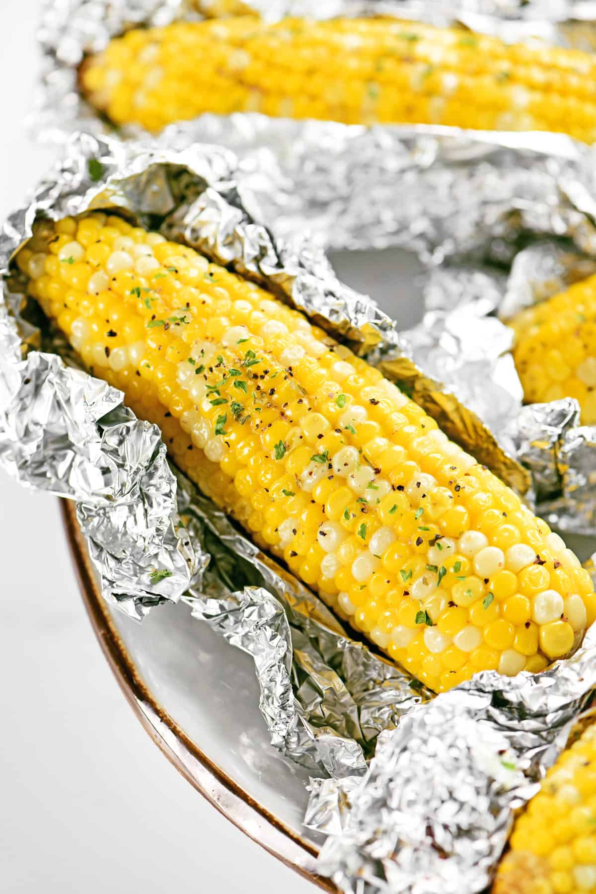 Grilled corn on the cob in foil with butter and herbs.