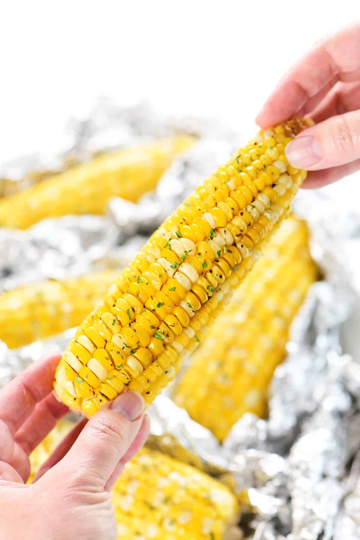 Hands holding a piece of corn grilled in foil.