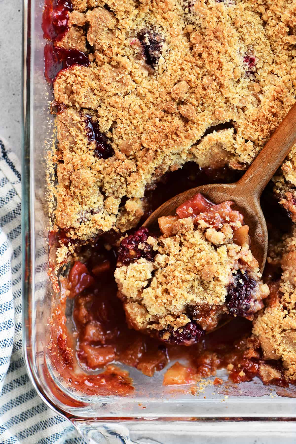 Apple and blackberry crumble in a pan with a wooden spoon.