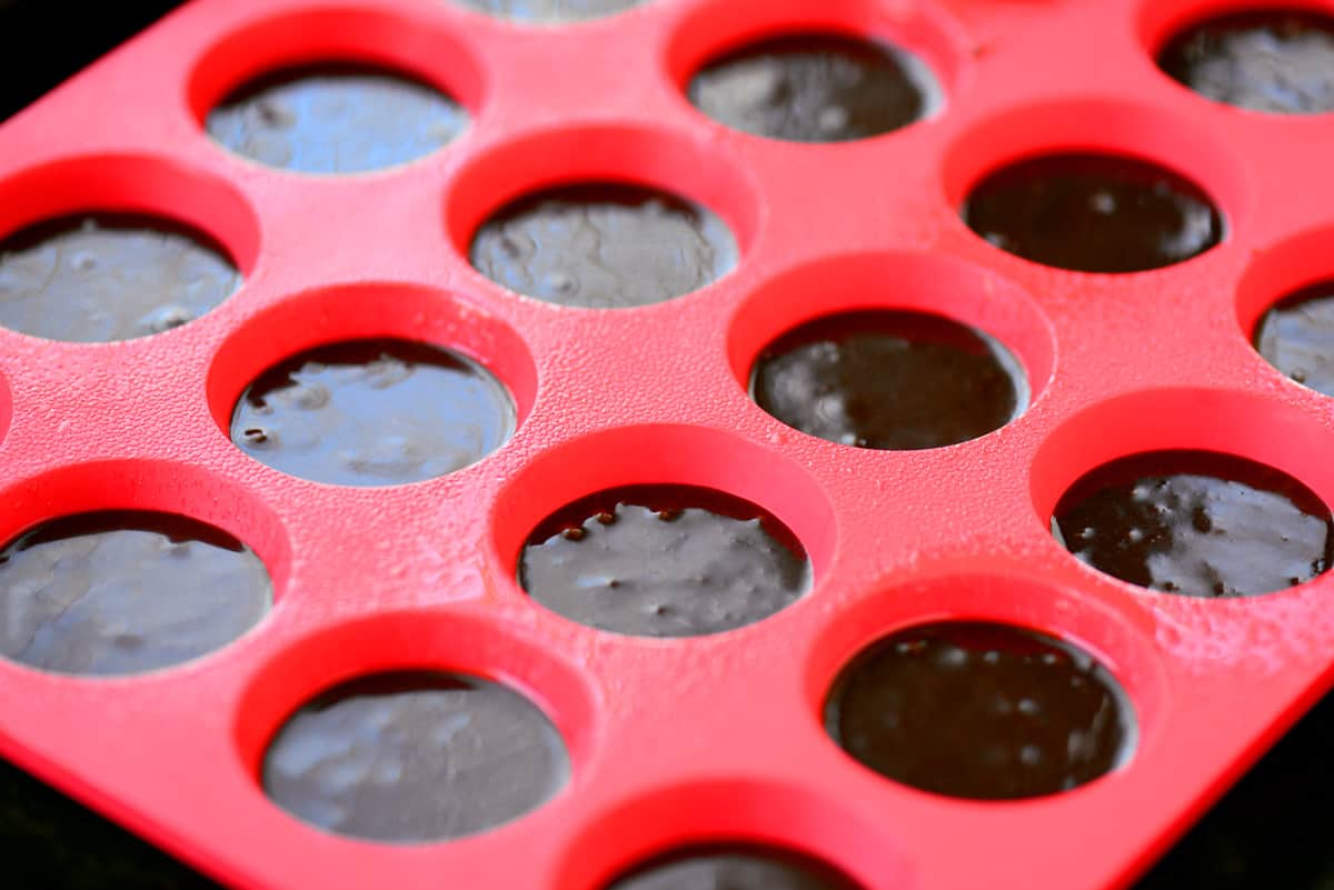 A red silicone mini muffin pan with brownie batter.
