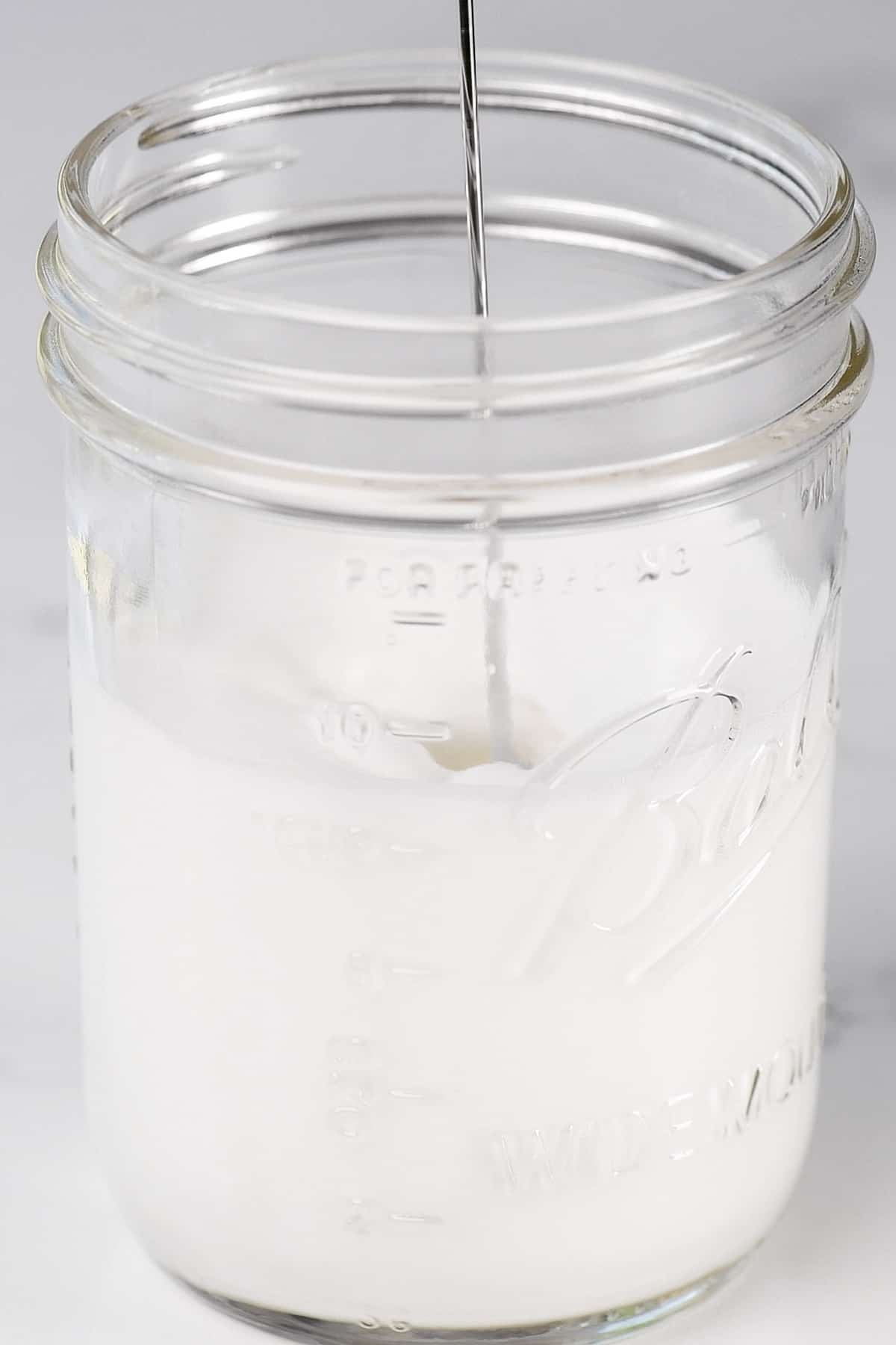 A frother making cold foam in a glass jar.