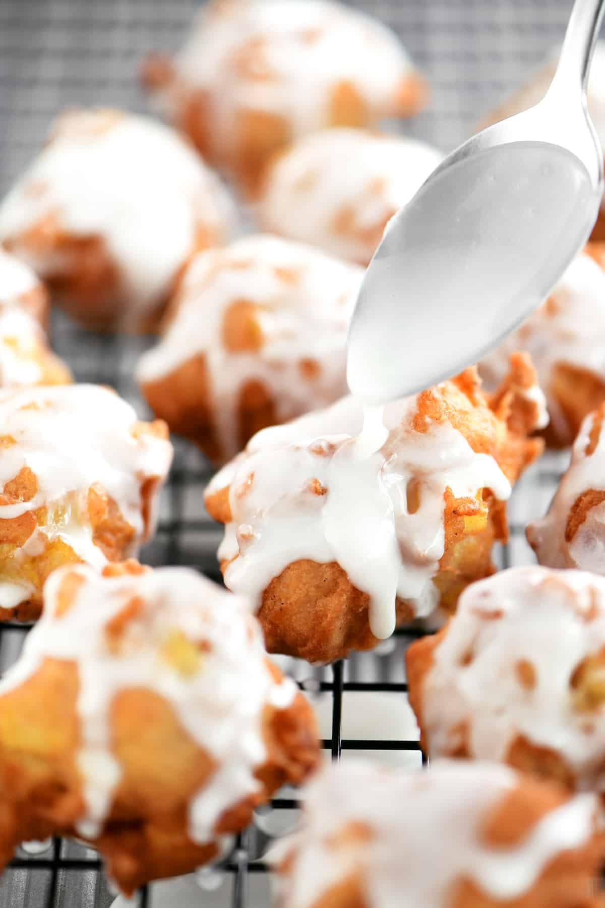 A spoon drizzling powdered sugar glaze on apple fritters.