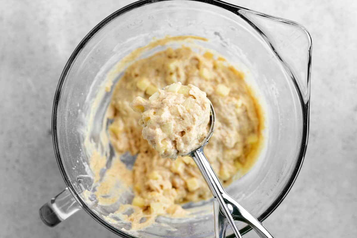 Scooping apple fritters batter with a dough scoop.