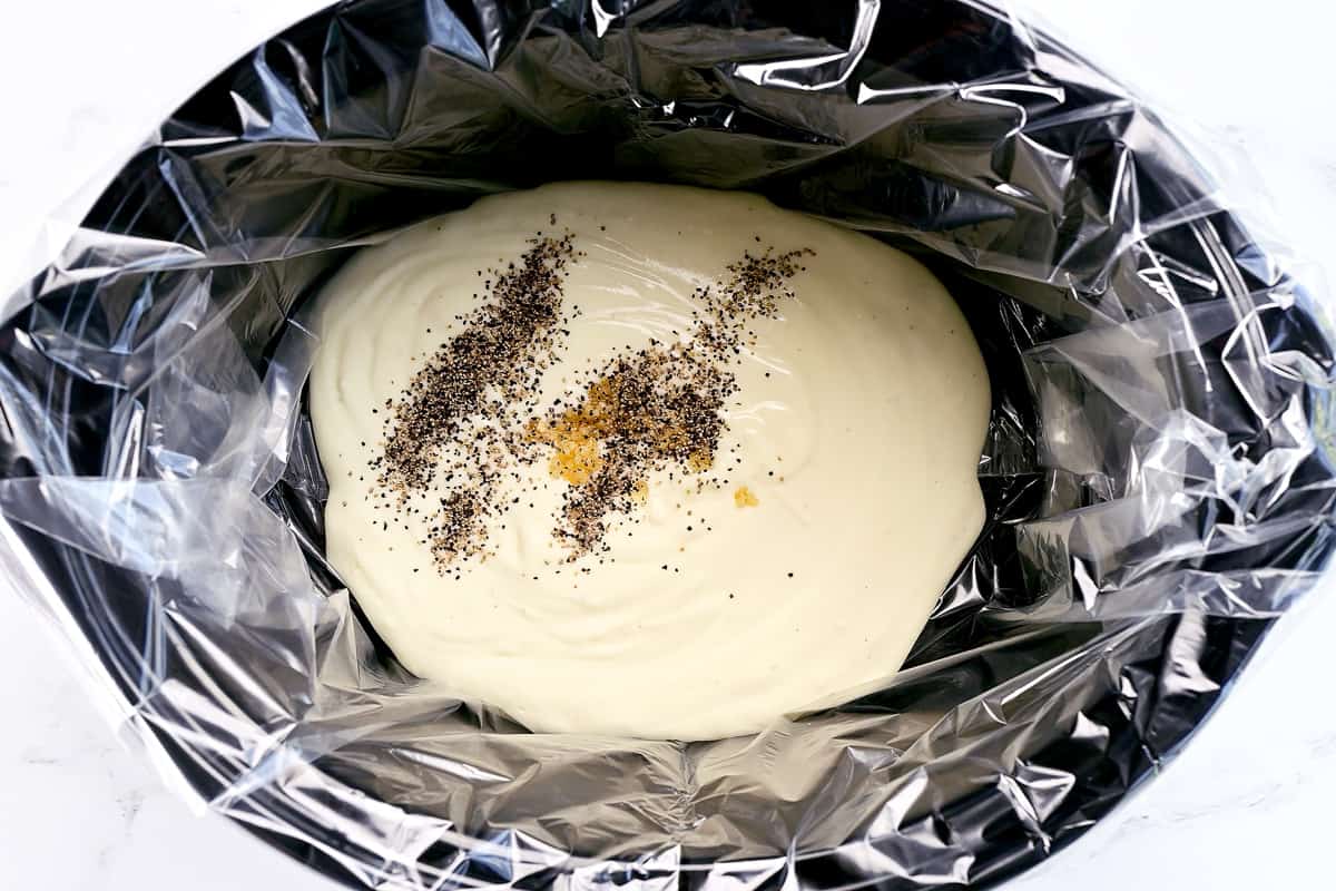 White creamy sauce and seasoning in a slow cooker.