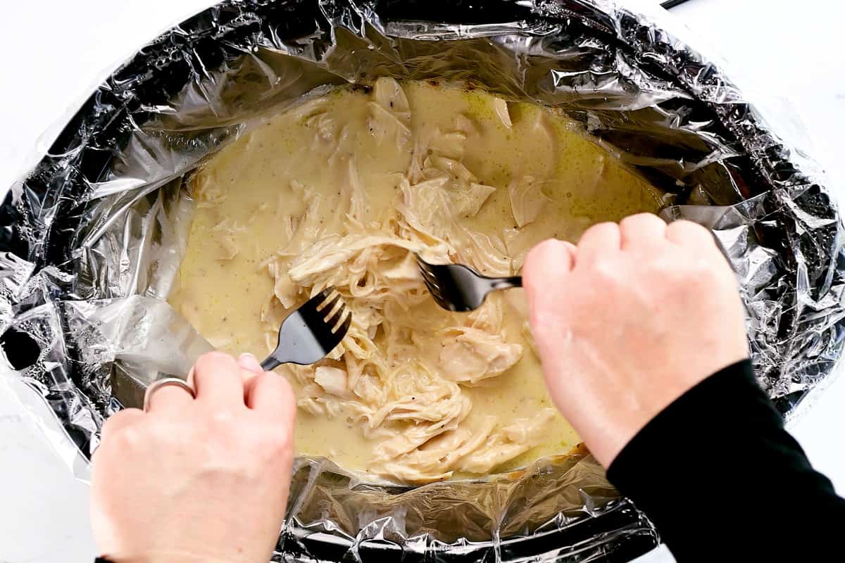 Using two forks to shred chicken in a slow cooker.