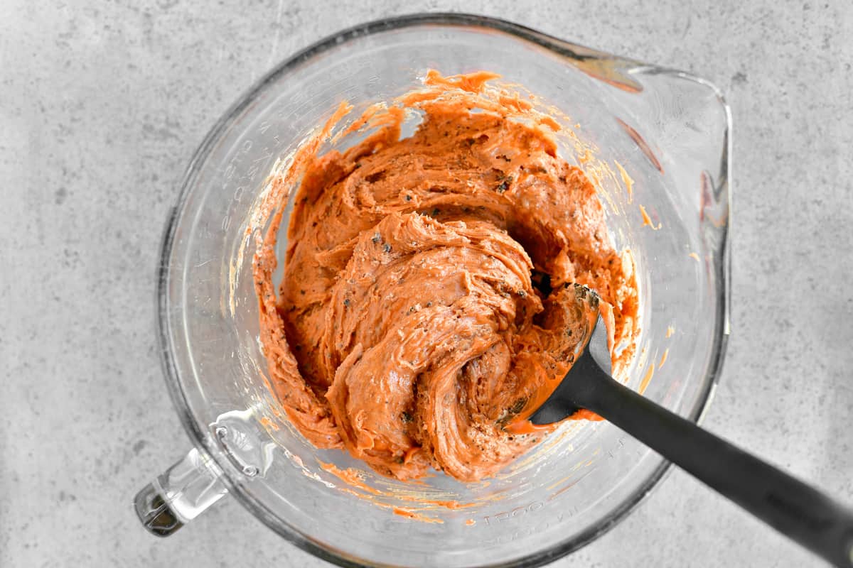 A black silicone spatula in a glass mixing bowl with orange fudge batter inside.