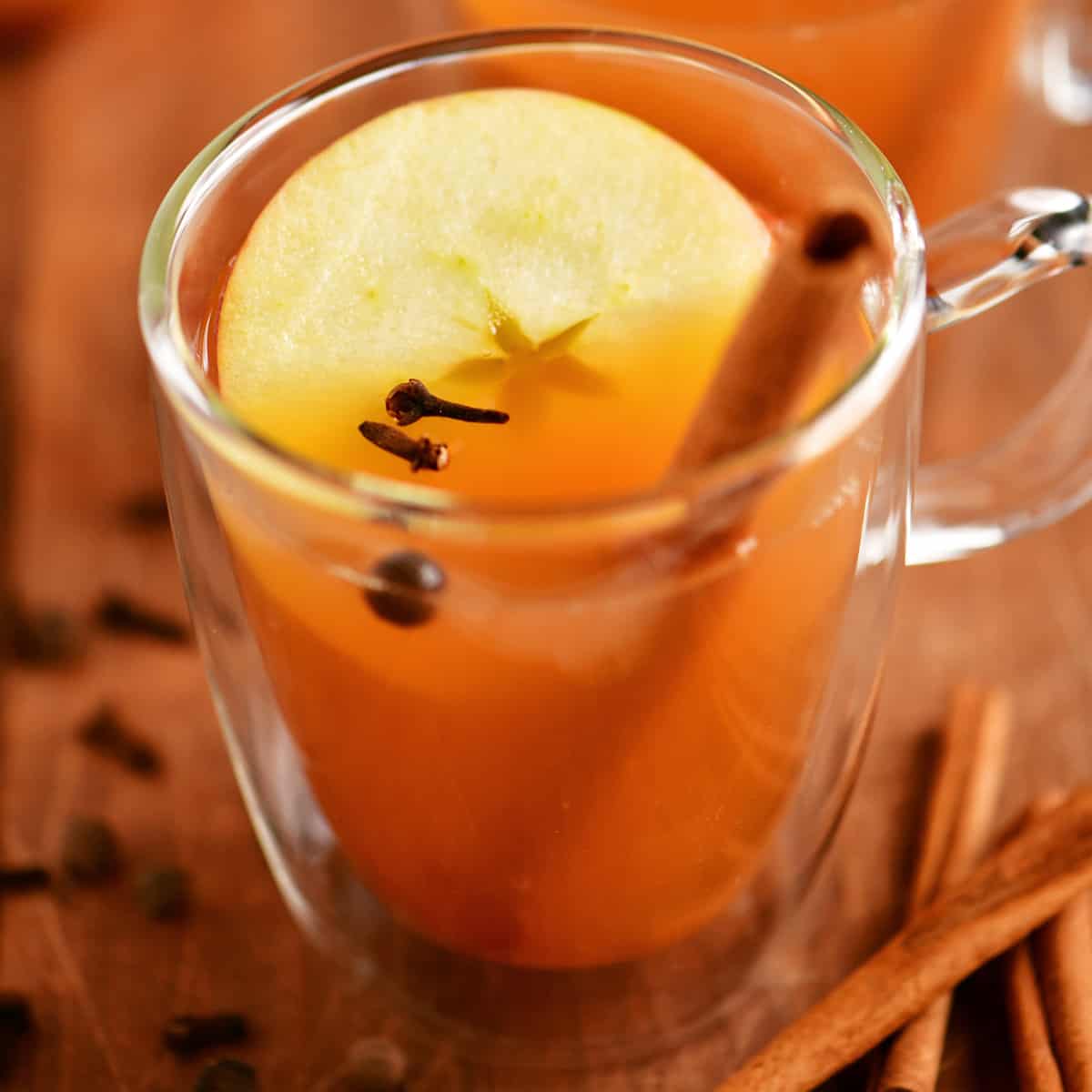 hot apple cider in a glass cup with an apple slice and mulling spices inside.