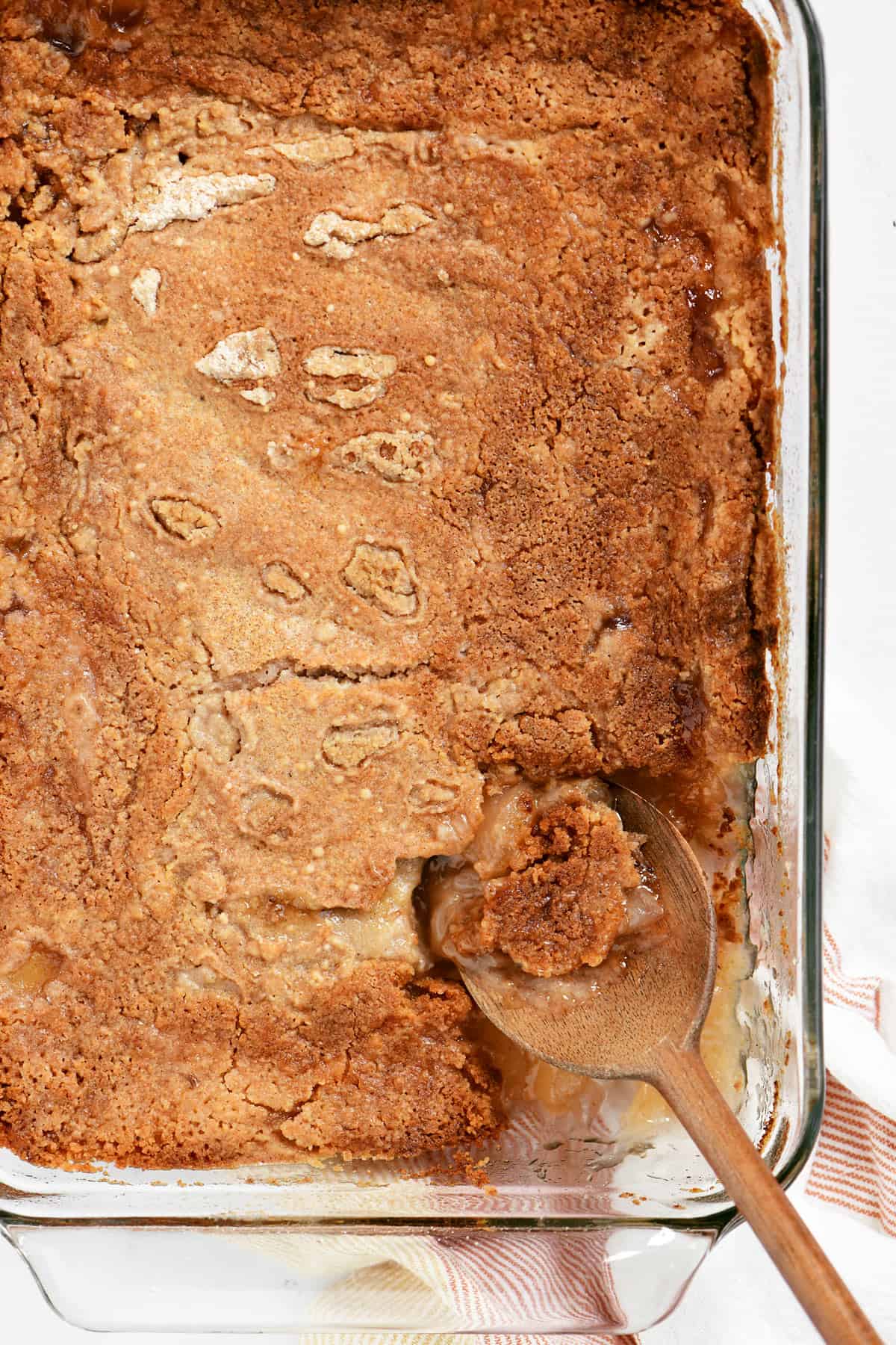 Bisquick apple cobbler in a pan with a wooden spoon.