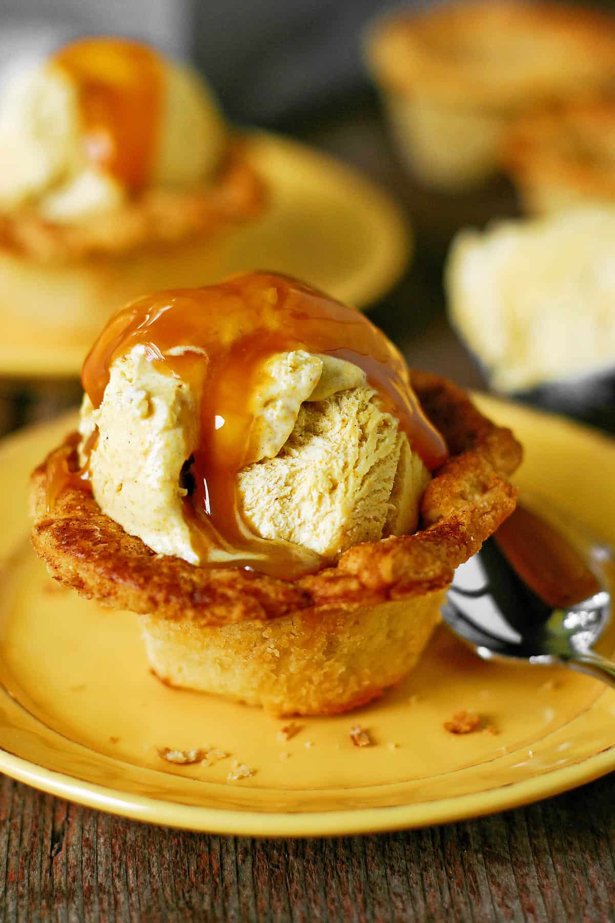 A scoop of pumpkin ice cream in a pie crust cup with warm caramel drizzled over the top.