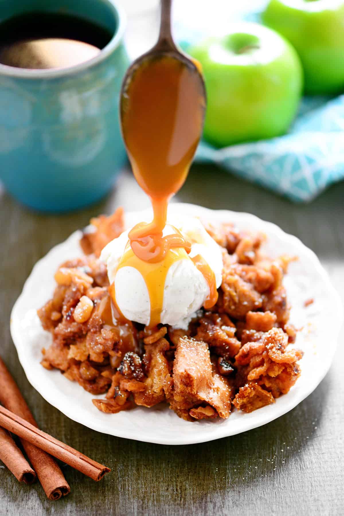 A spoon drizzles melted caramel syrup on ice cream and apple bread pudding.