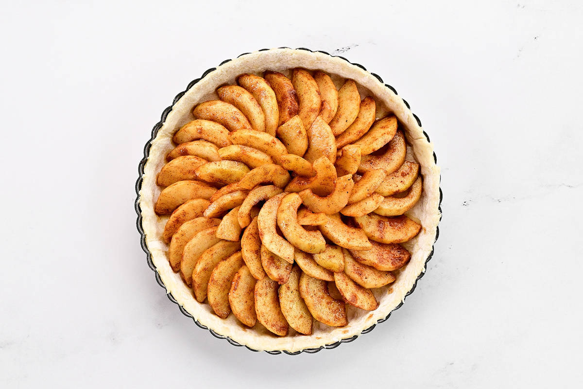 Apples arranged in a circle in a puff pastry in a tart pan.