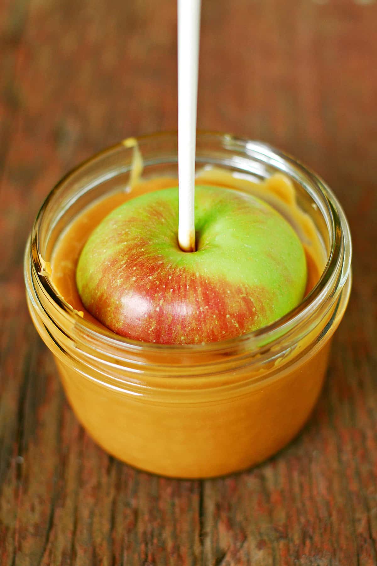 An apple on a stick dipped into melted caramel in a jar.