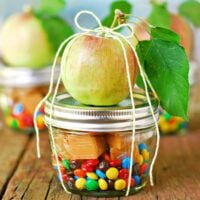 An apple on top of a glass jar filled with caramels and candy.