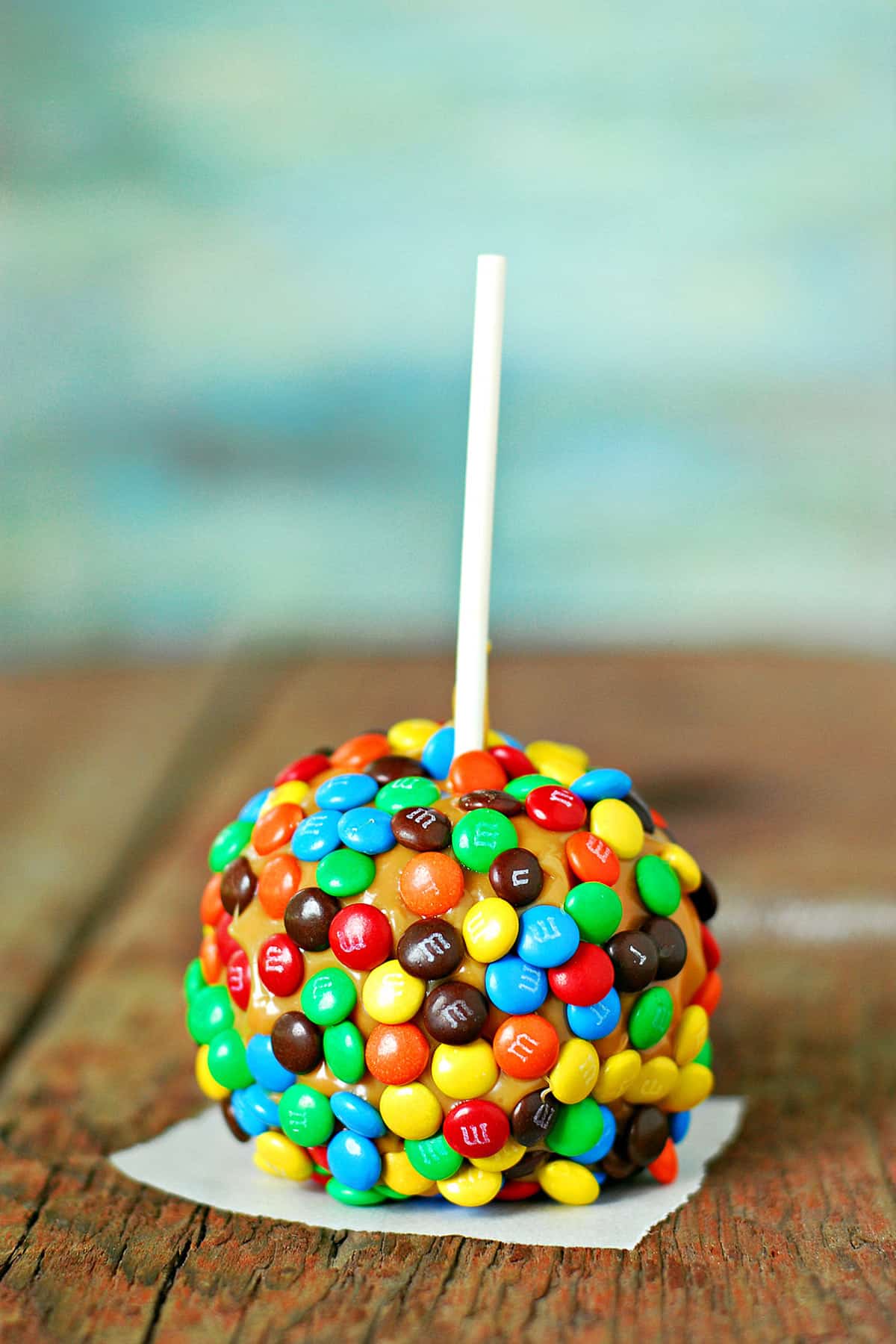 A caramel apple with M&Ms candy covering it.