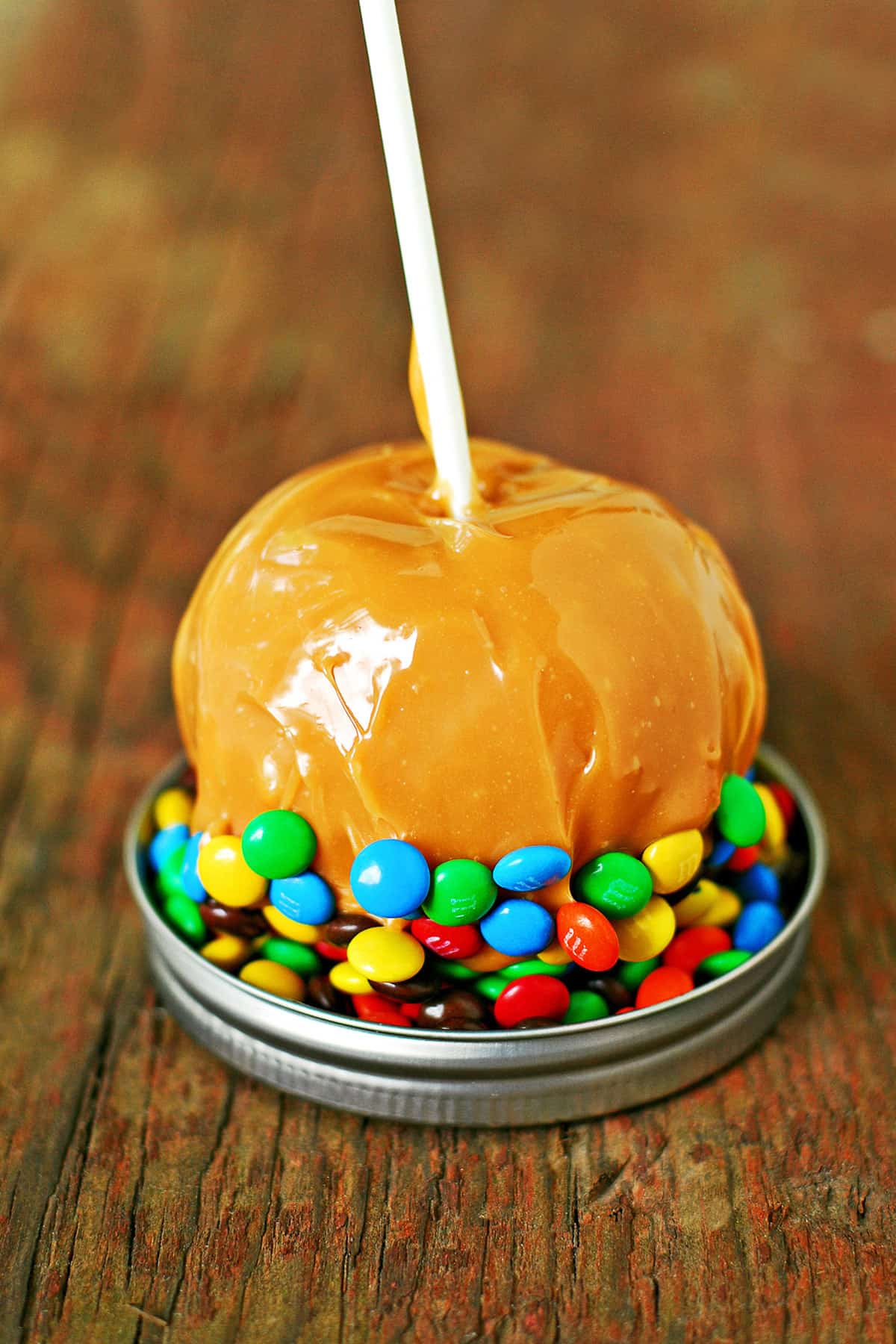 A caramel apple dipped into candies in a jar lid.