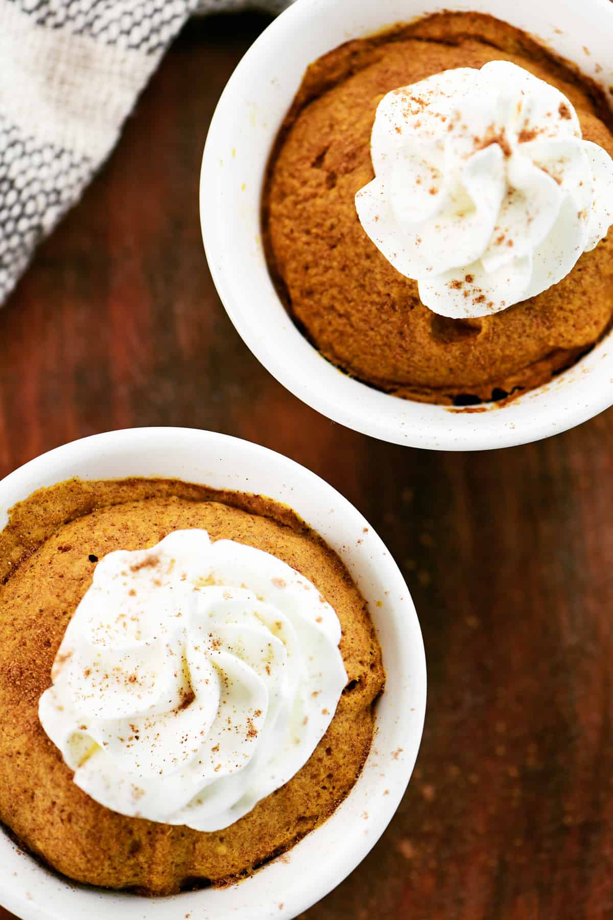 Two pumpkin mug cakes with whipped cream on top.