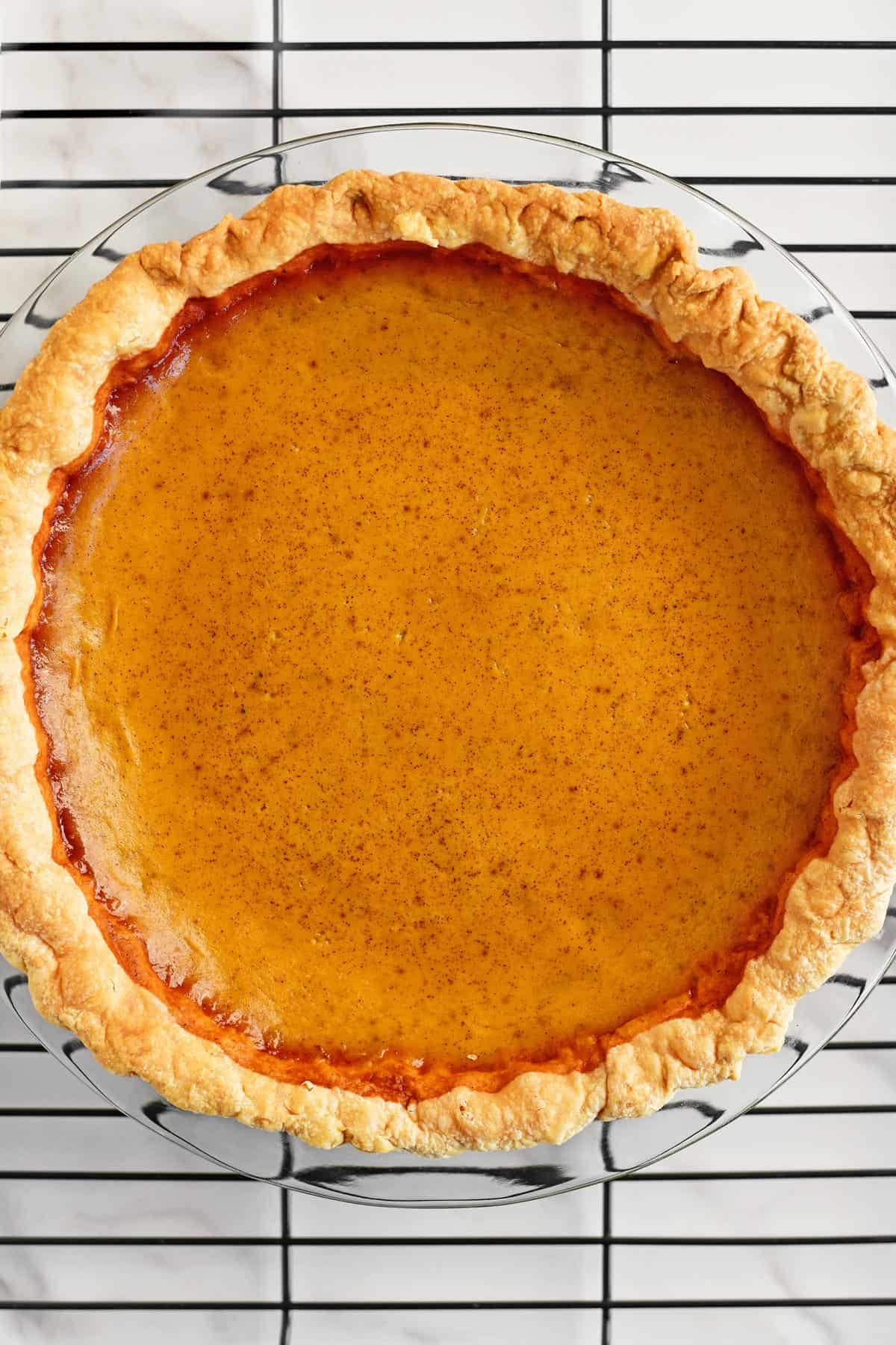 A baked pumpkin pie on a cooling rack.